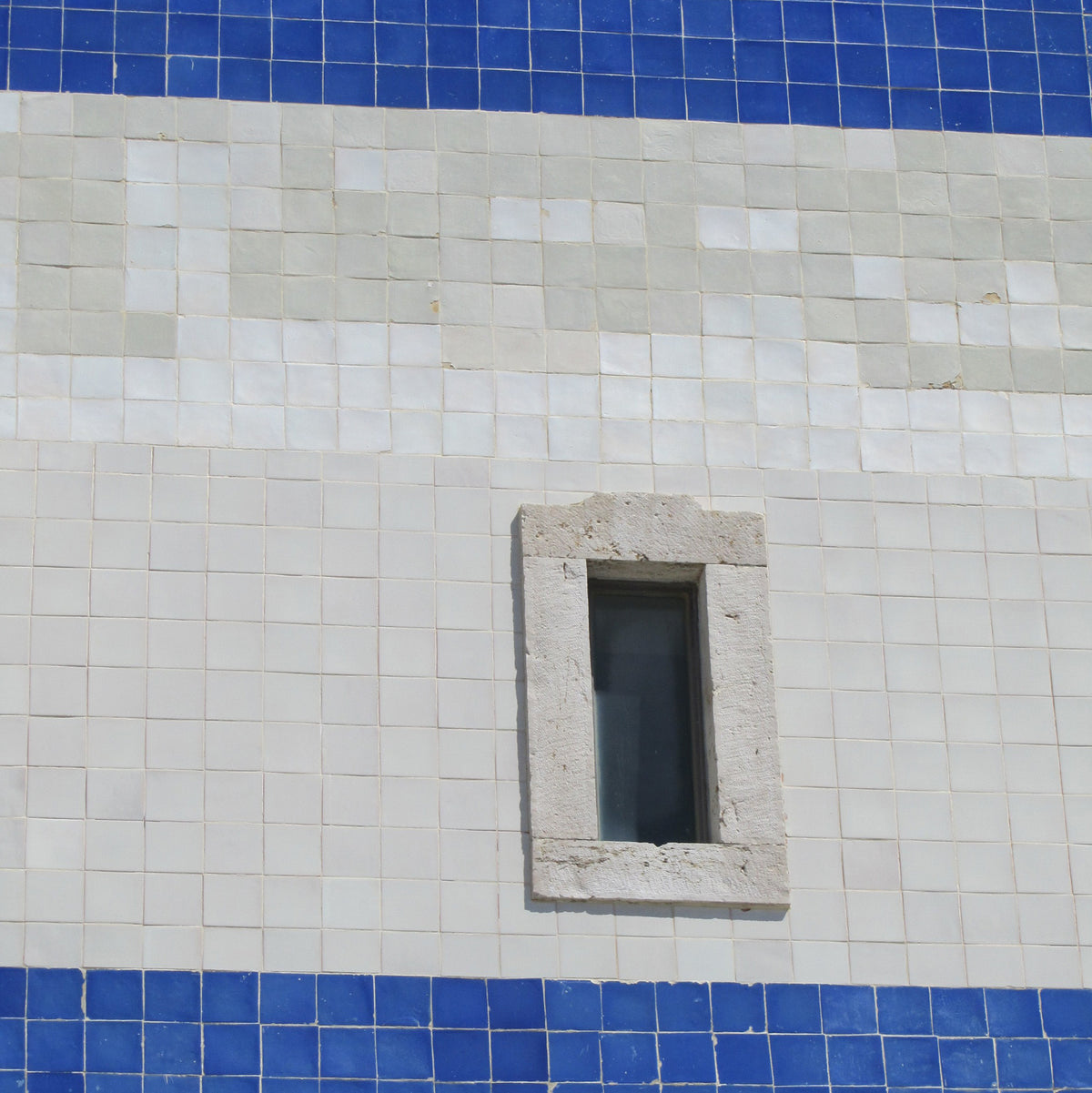 a window on the side of a building surrounded by white tile