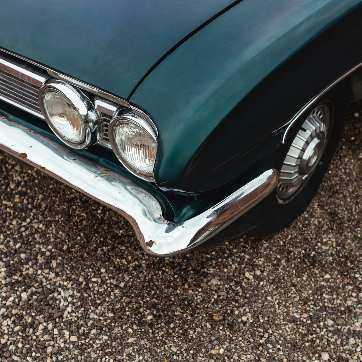the front end of a classic blue car on a driveway