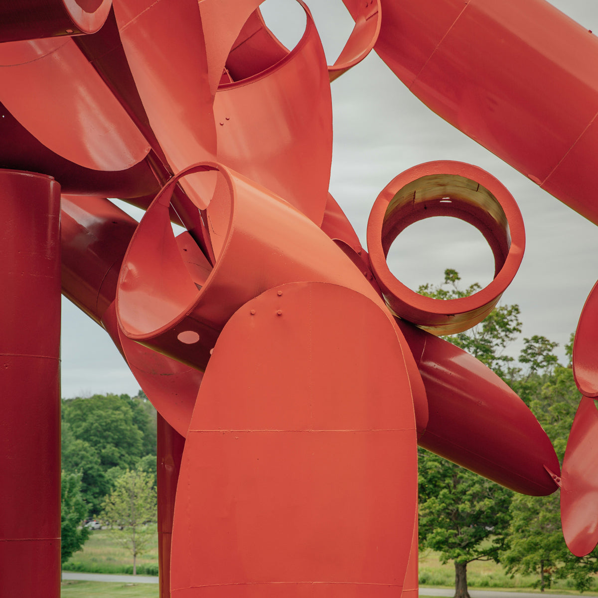 a red metal sculpture having curves and round tubes displayed outdoors