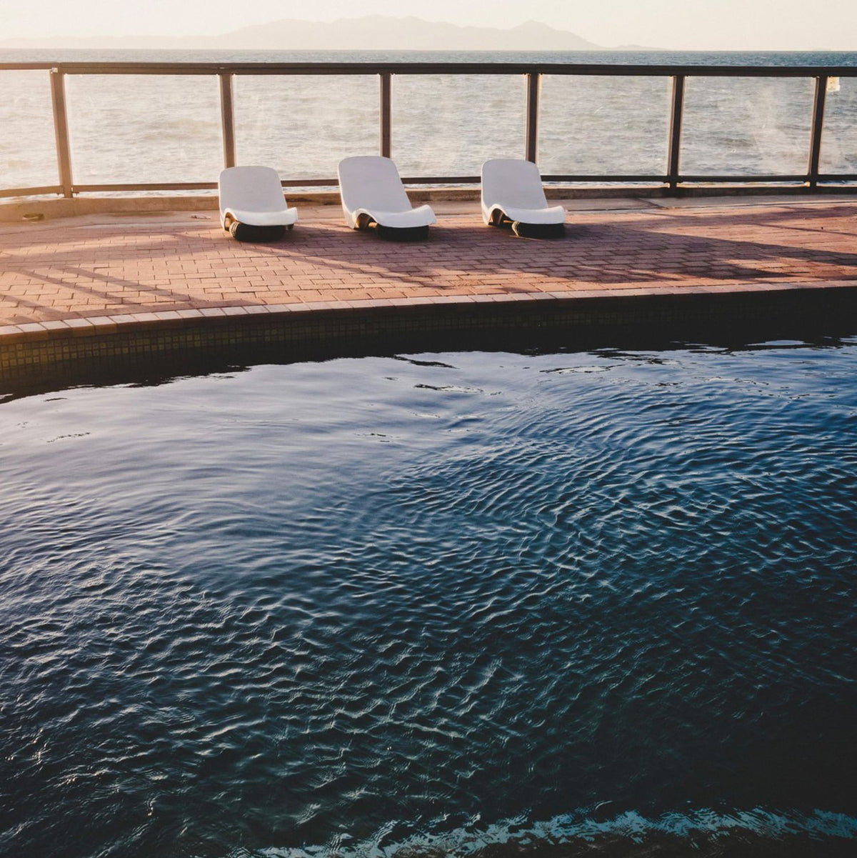 three white lounge chairs on a deck next to a pool
