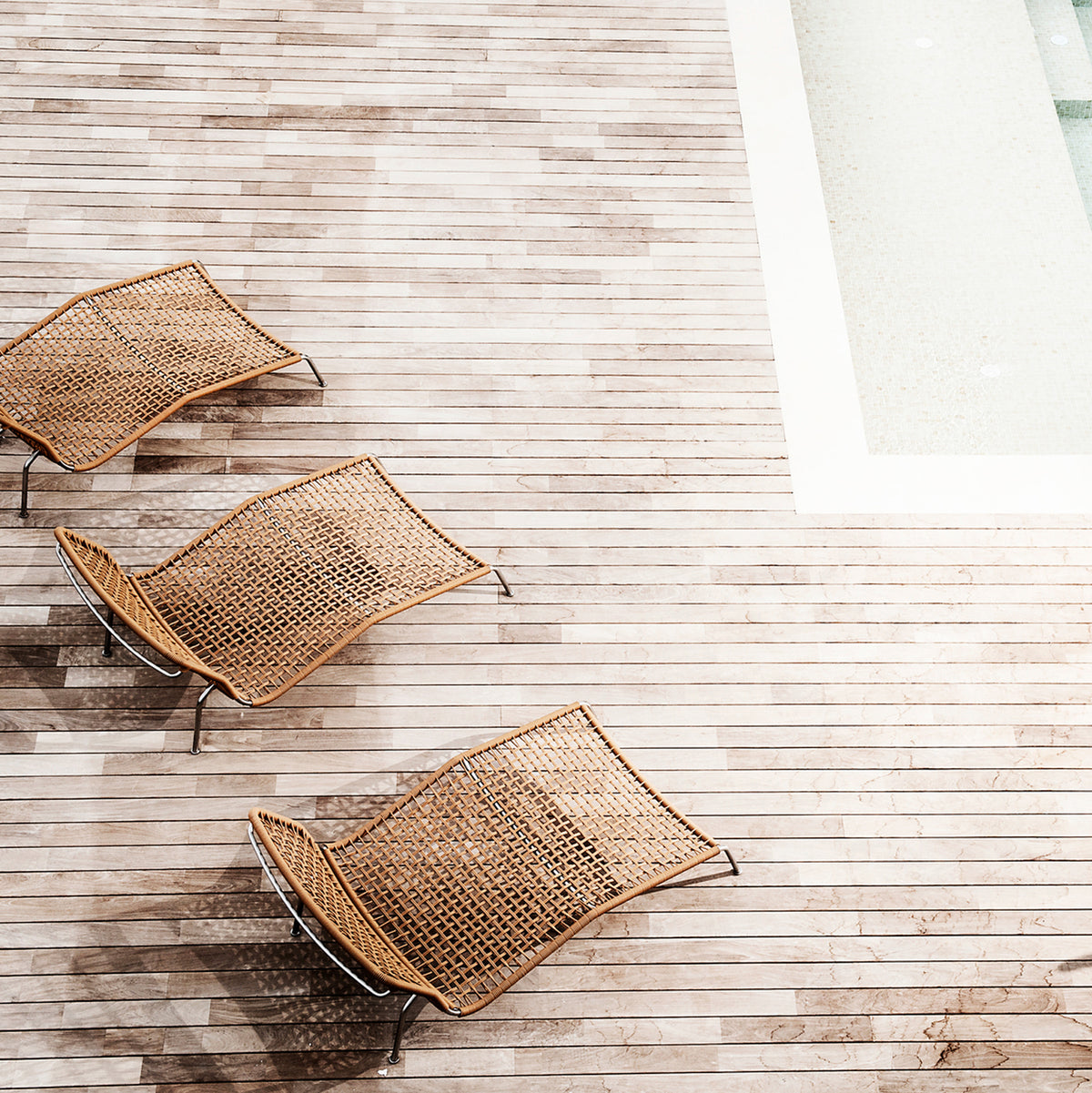 three brown rattan lounge chairs on a deck next to a pool