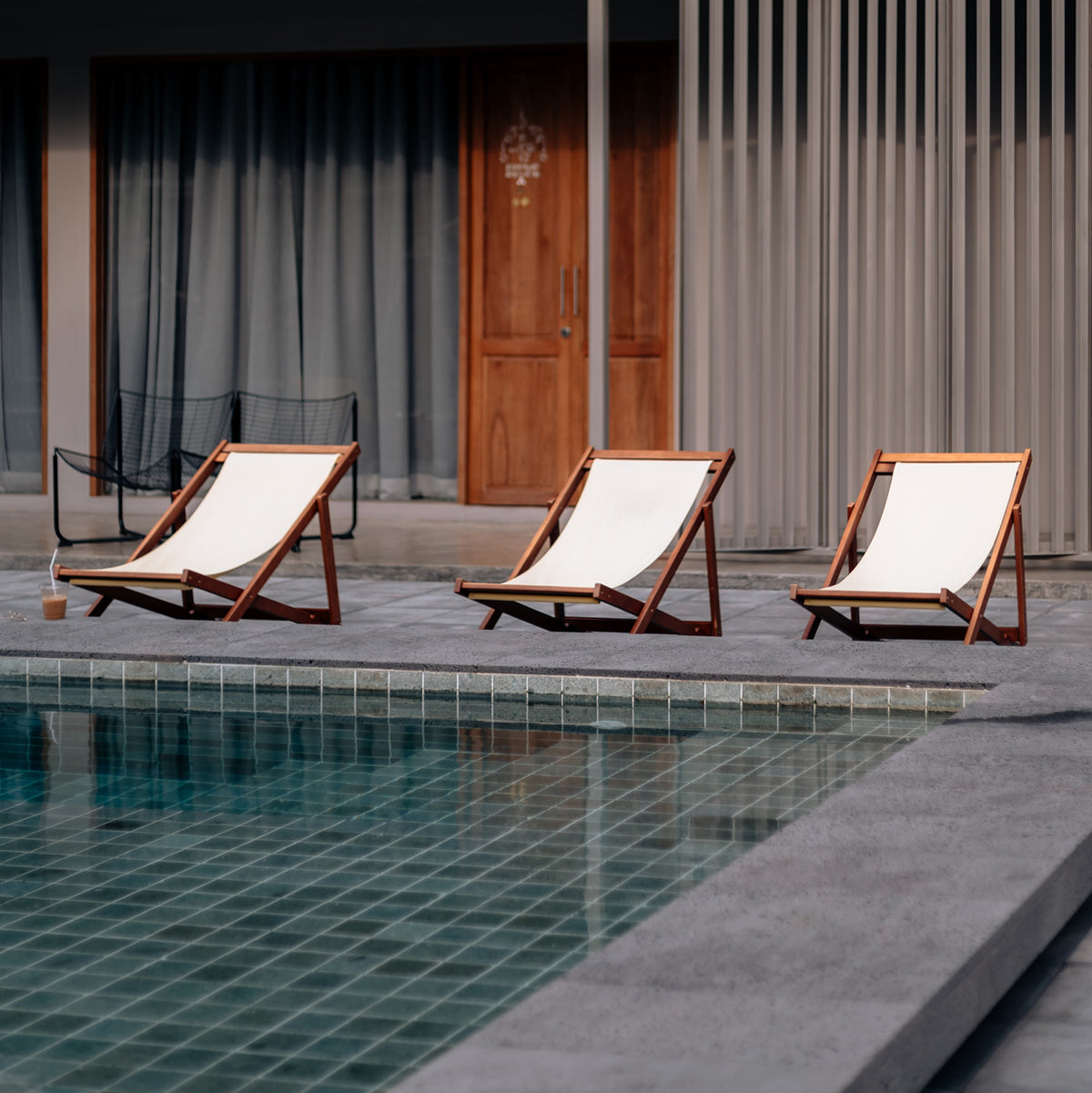 three white linen folding lounge chairs next to a pool